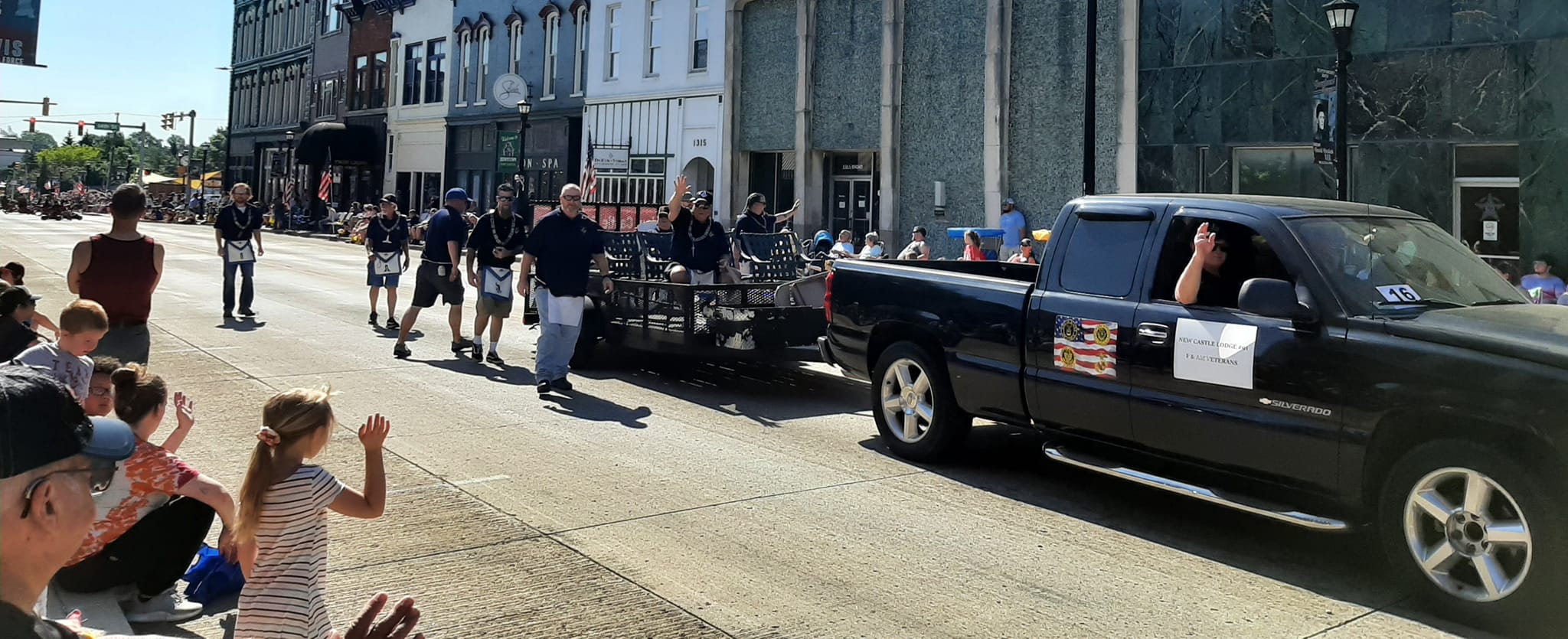 A black truck pulling a trailer in a parade, men walking beside trailer