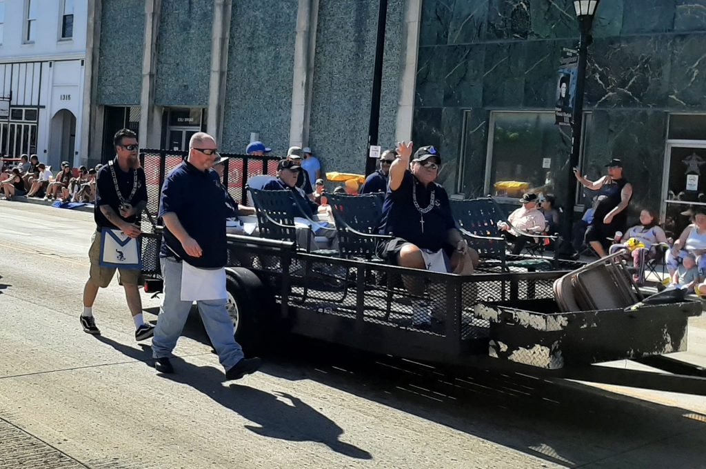 Freemasons riding in a black trailer in a parade.